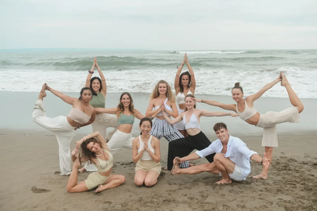 300 Hours Yoga Teacher Training 2 Group of yoga teacher training students in Bali performing advanced yoga poses on the beach during 200 hour certification retreat.